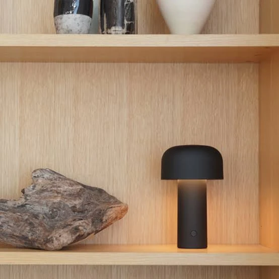 Flos Bellhop portable lamp in matt black on a wooden shelf beside a piece of driftwood