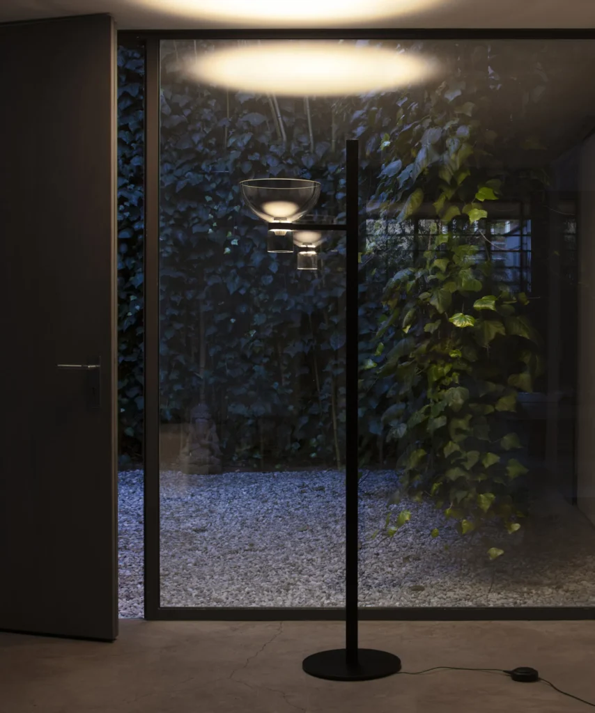 Flos Nocturne Floor Bowl lit at night in front of a glass wall and a planted courtyard