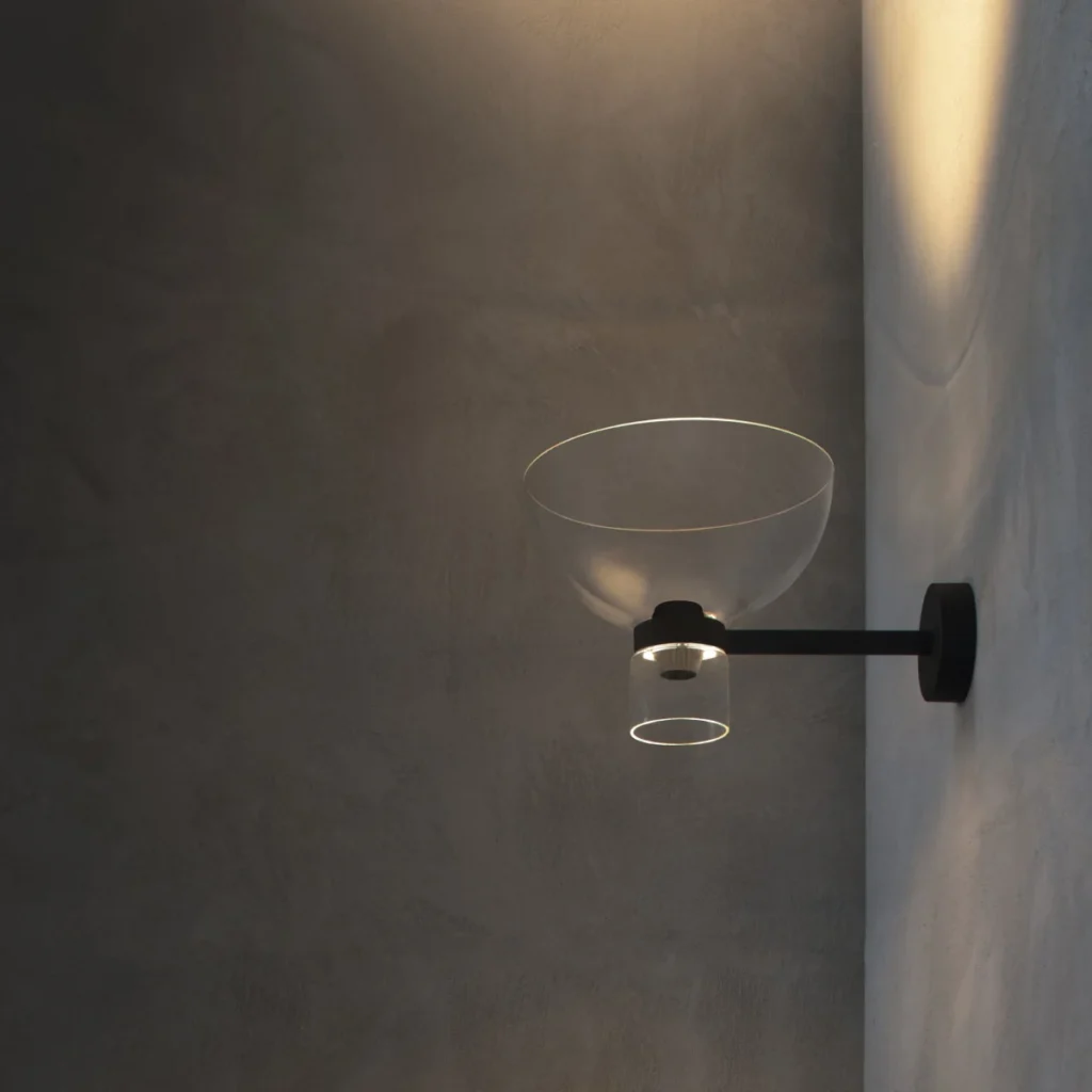 Flos Nocturne Wall Bowl lit on a dark plaster wall